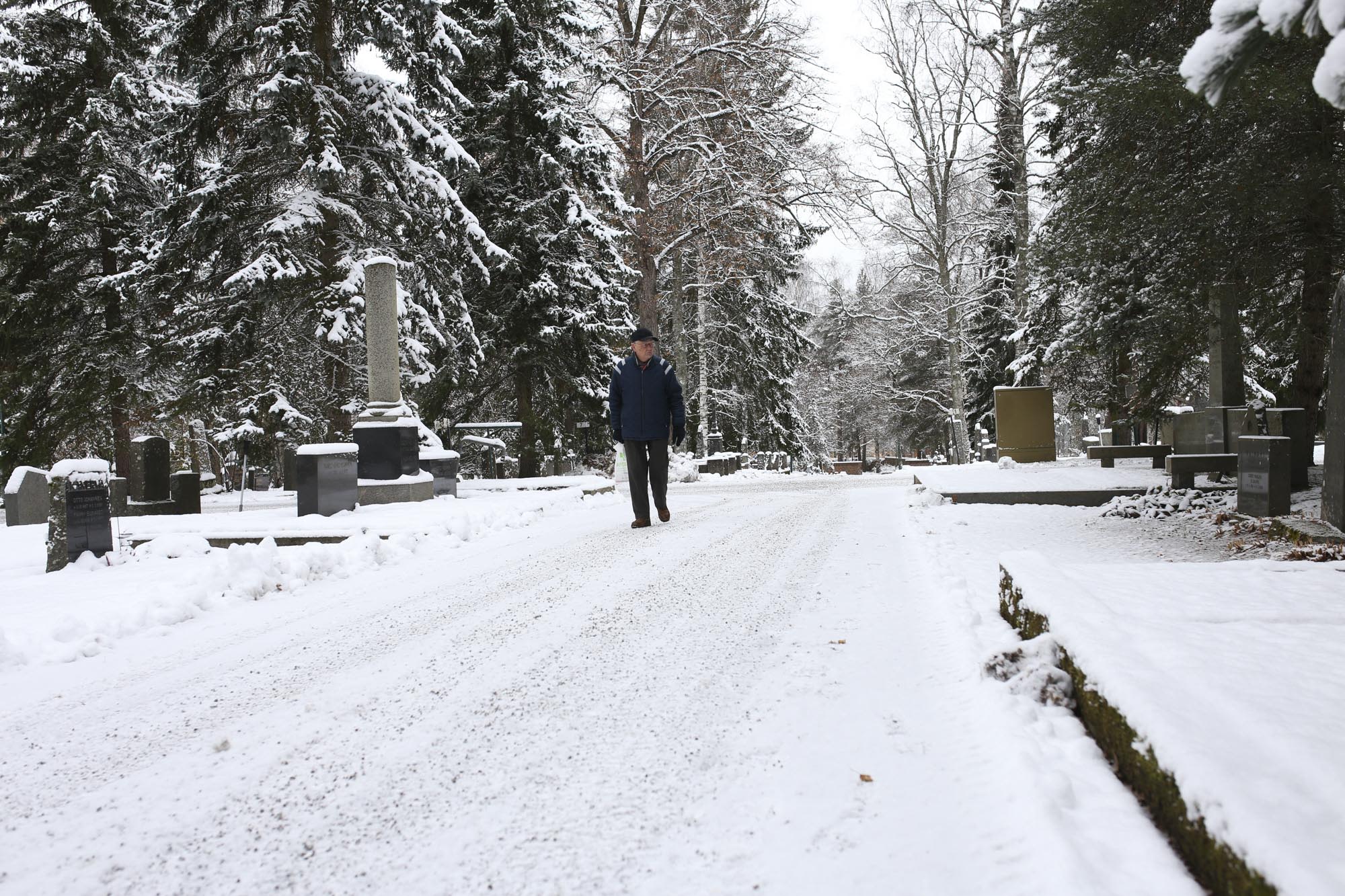 Mies kävelee lumisella hautausmaan polulla.