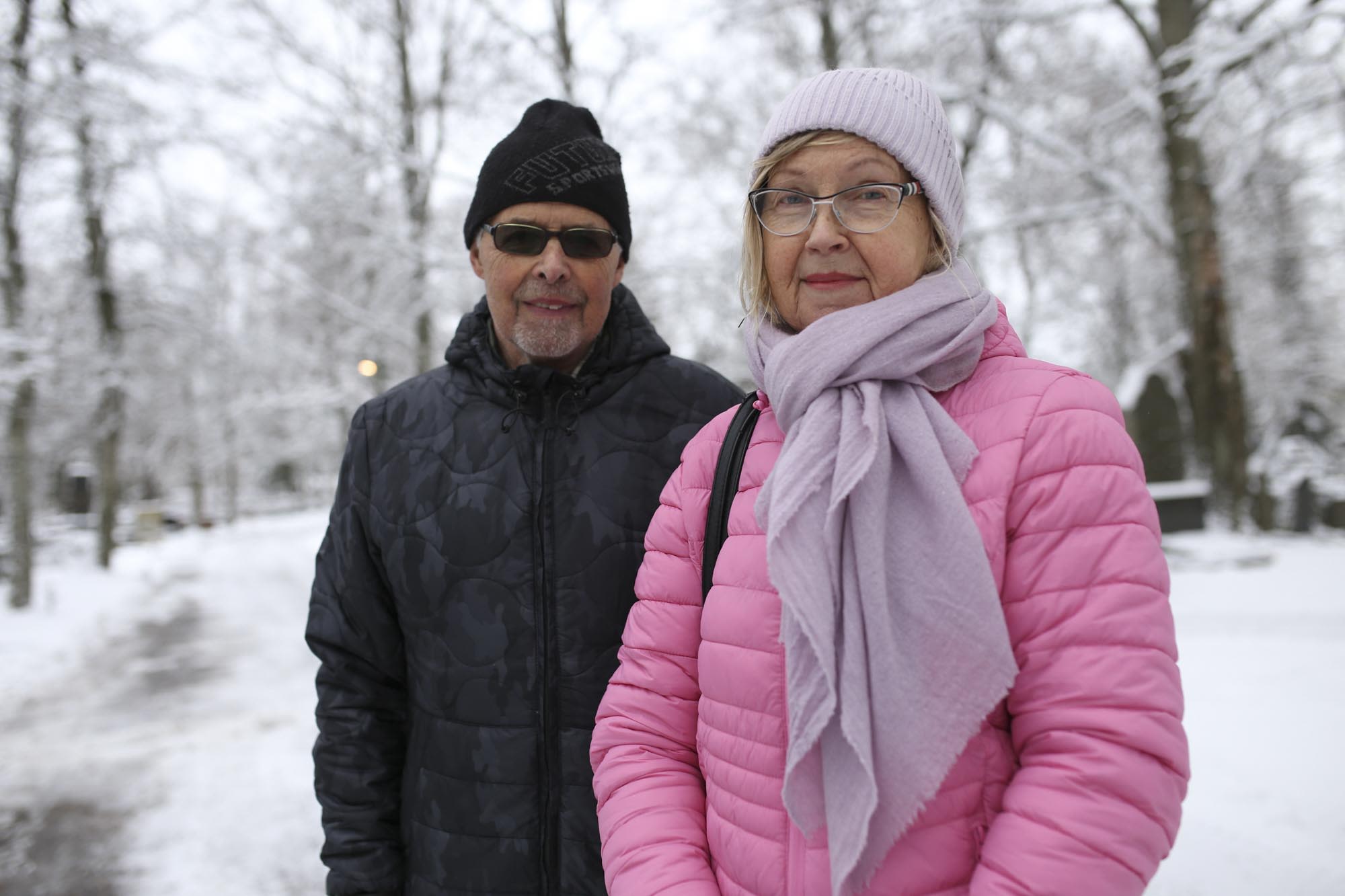 Mies ja nainen katsovat kohti talvisella hautausmaalla.