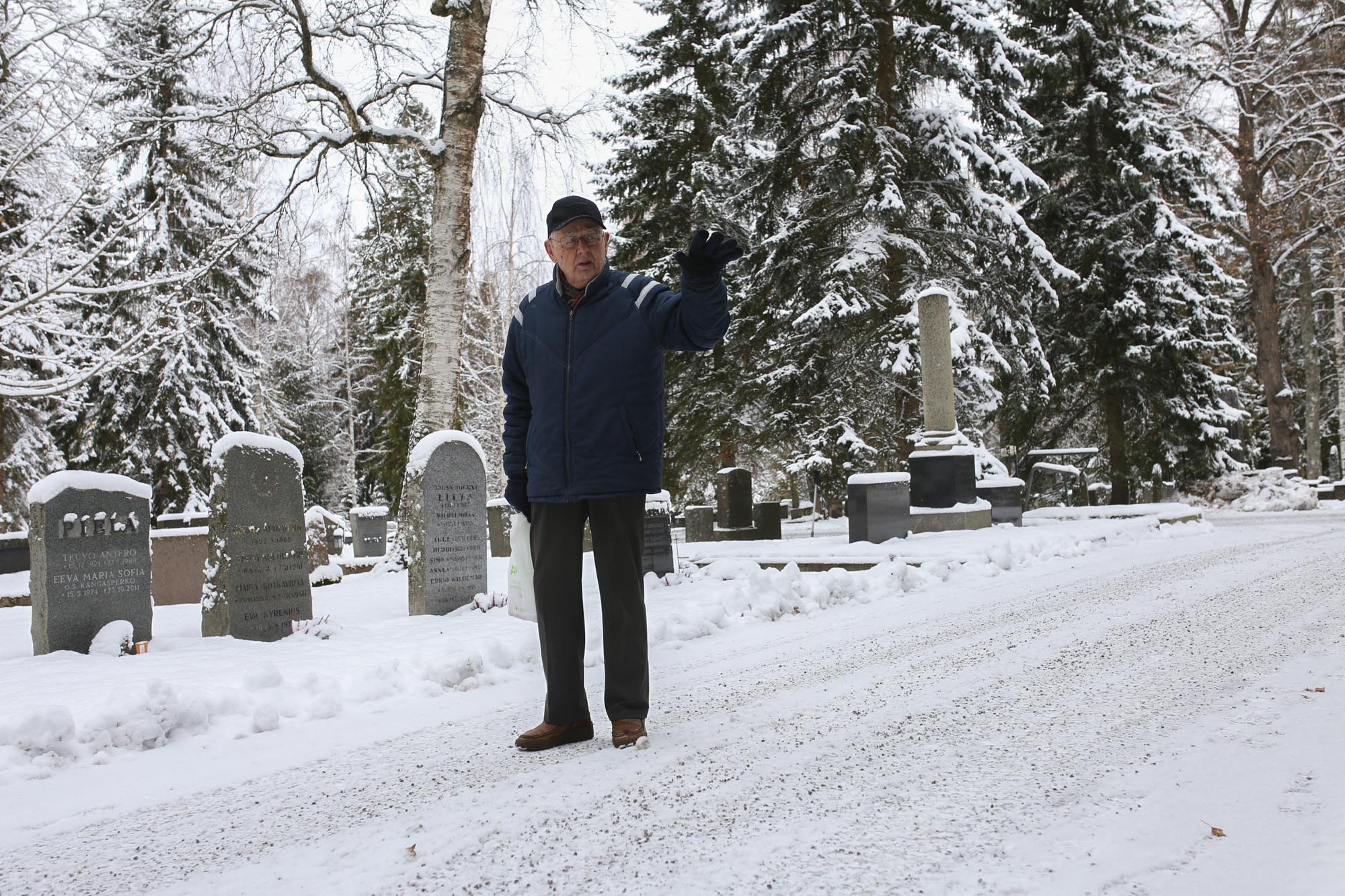 Mies seisoo hautausmaan polulle ja viittelöi kädellään.