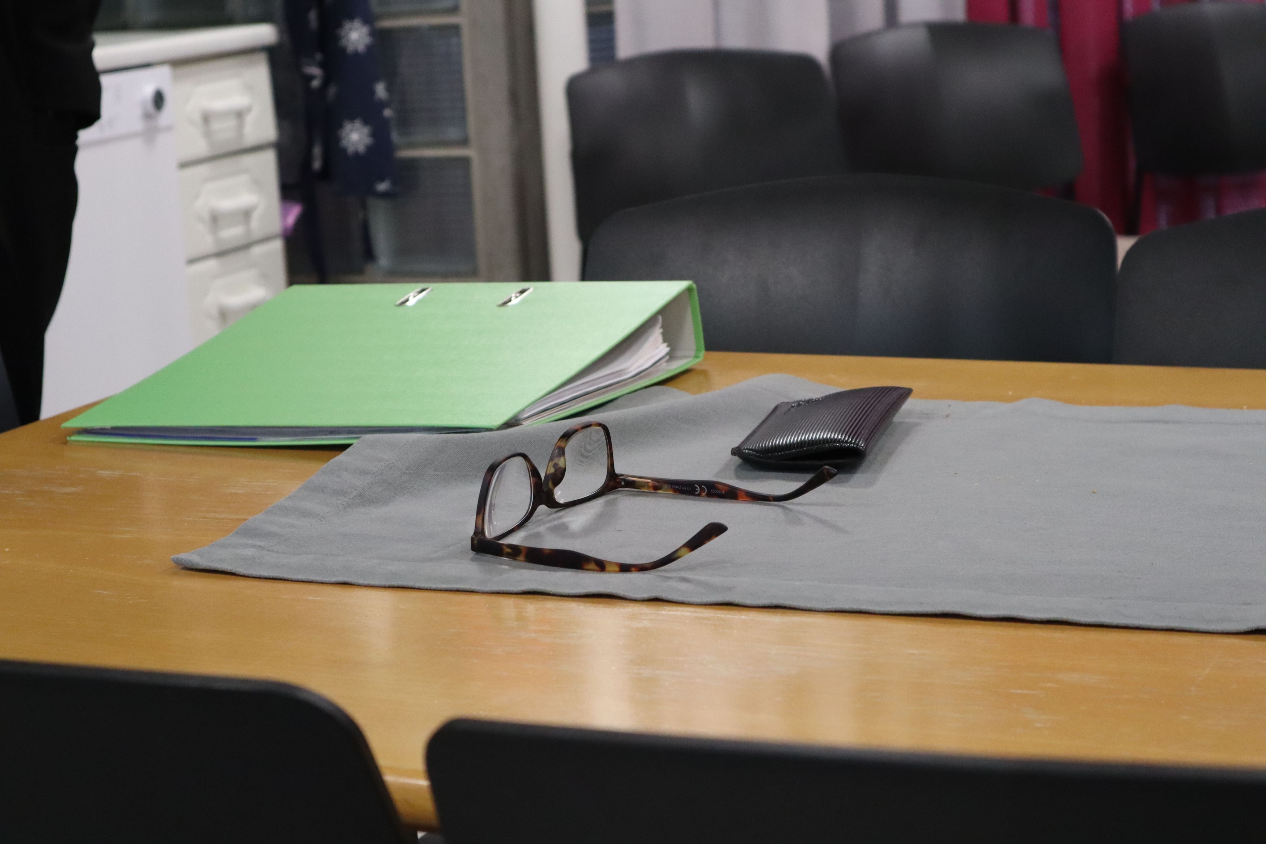 Pöydällä silmälasit, kansio ja lompakko.