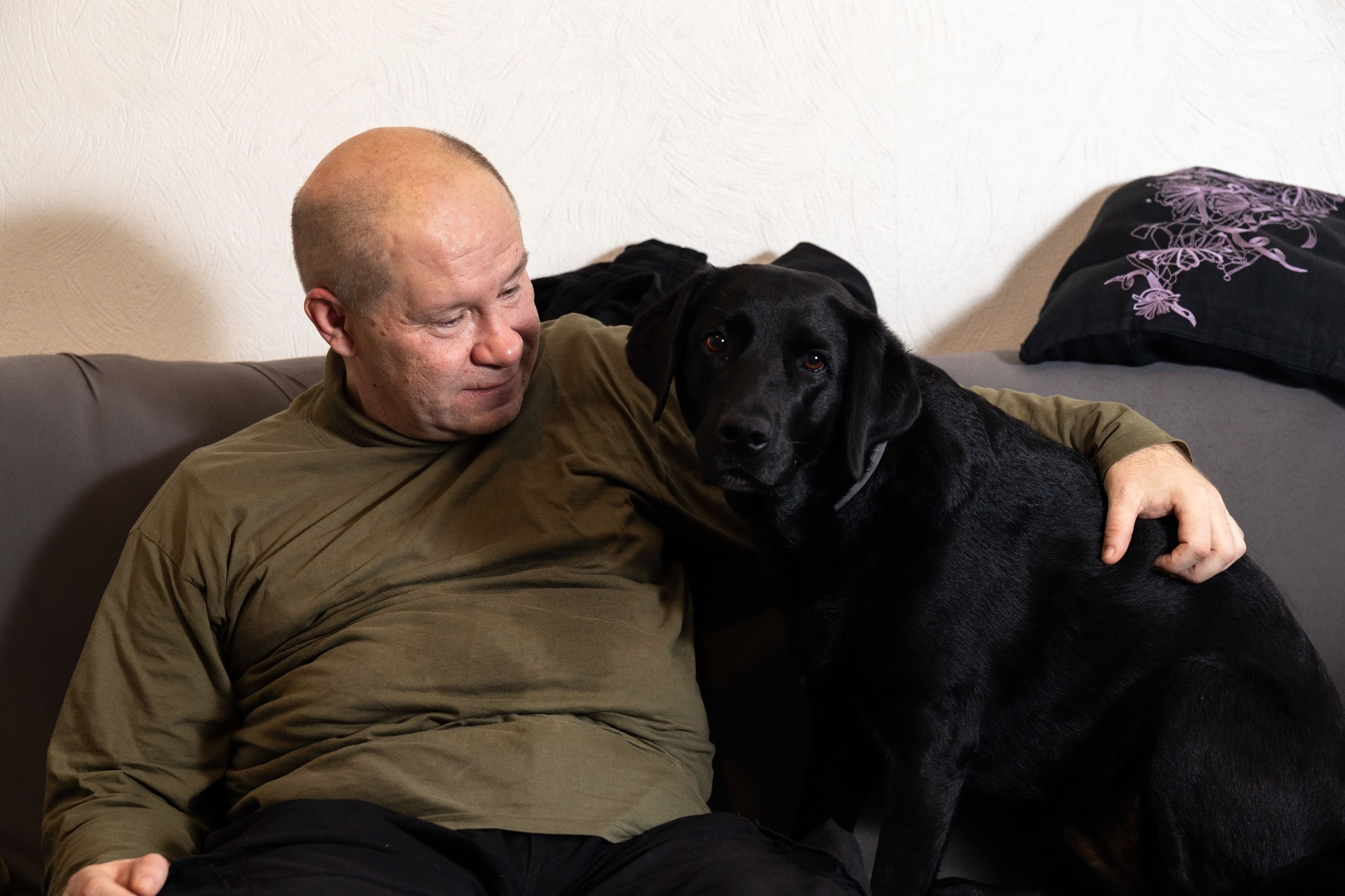 Tommi Jyväkorpi ja Talvi-koira istuvat sohvalla. Tommi katsoo Talvia hymyillen, ja Talvi katsoo kameraan.