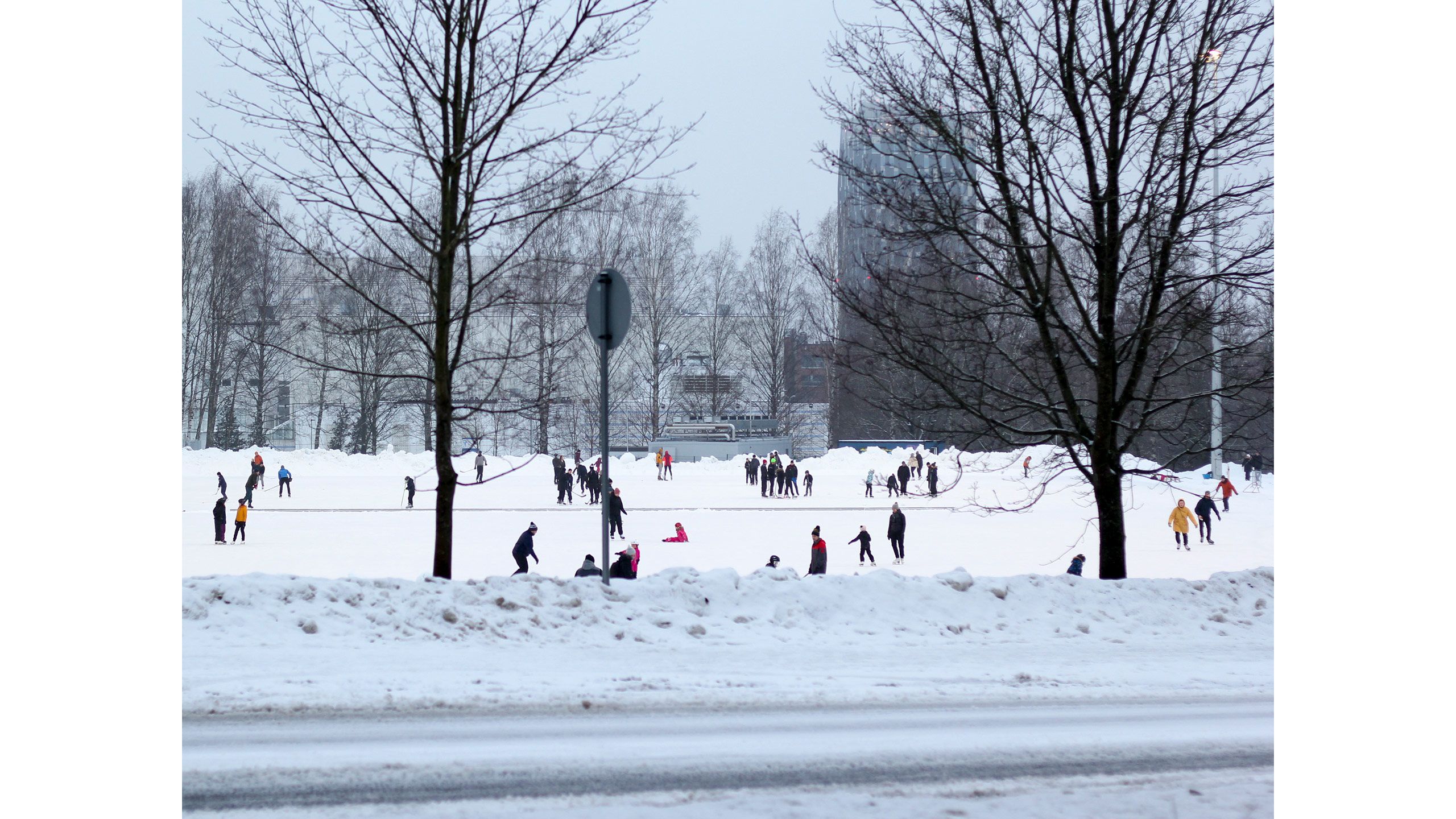 Joukko ihmisiä luistelemassa suurella luistelukentällä. Yksi luistelijoista on kellahtanut kumoon jäälle.