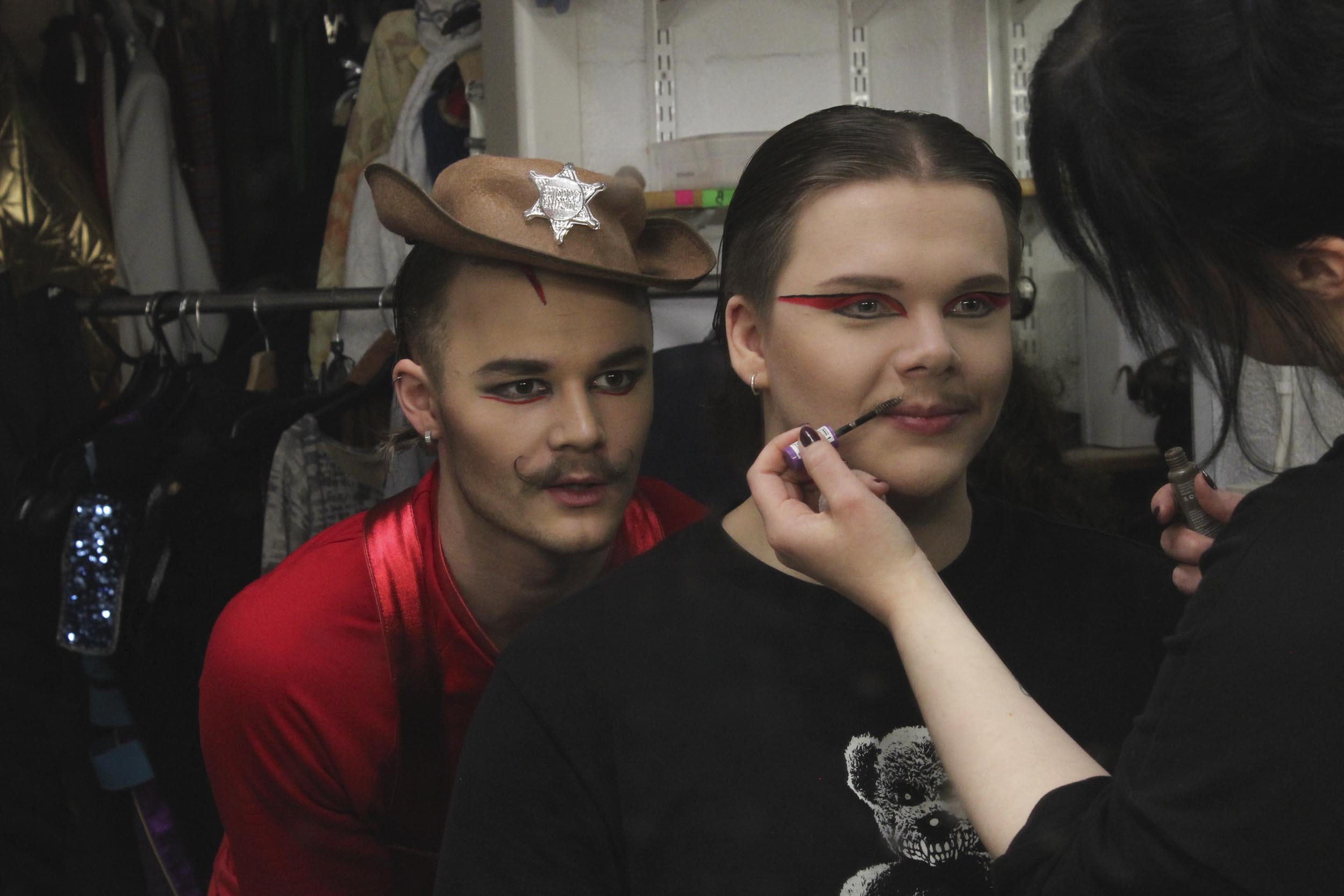 Maskeeraaja lisää vahaa esiintyjän viiksiin.