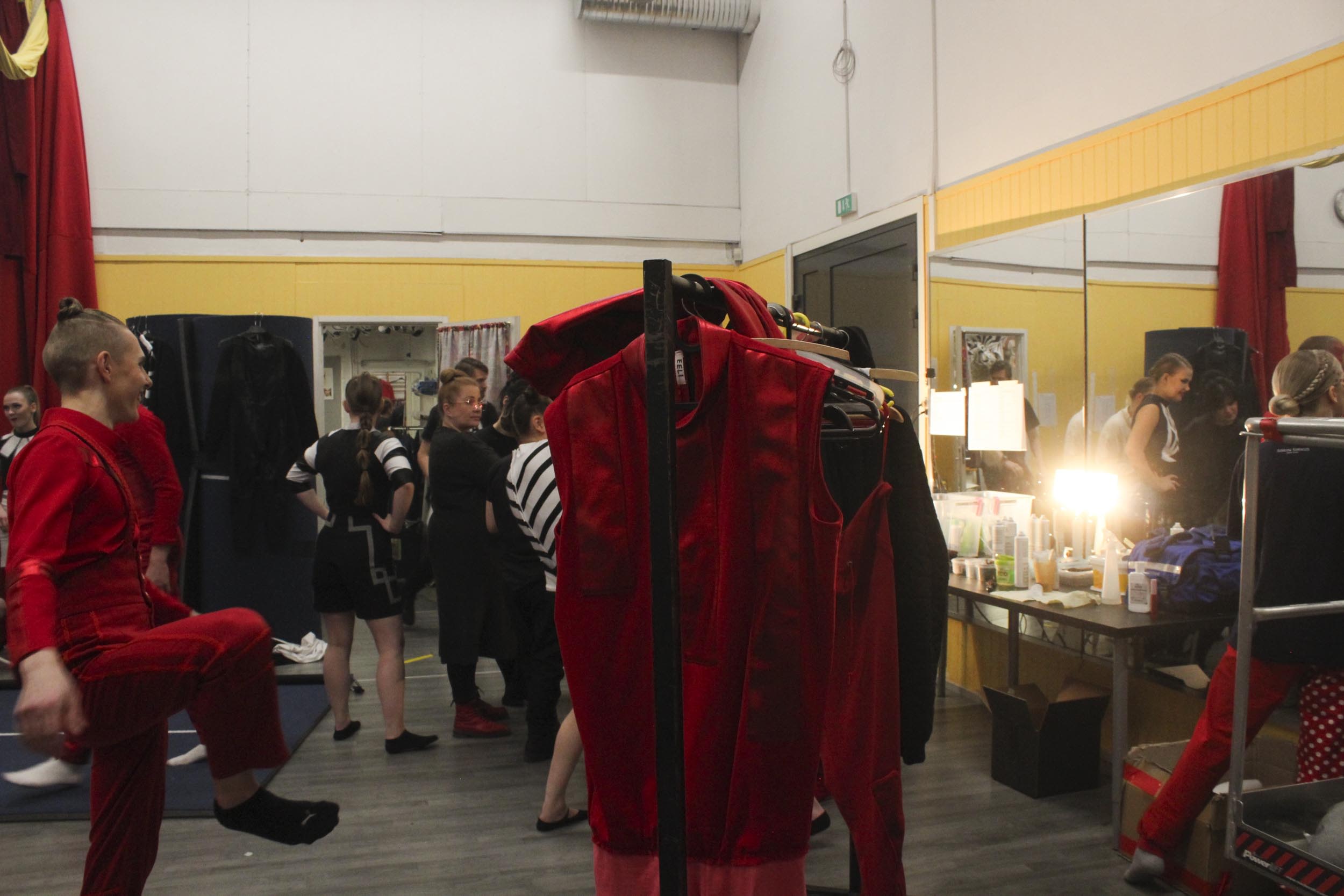 Näkymä Sorin Sirkuksen joulunäytöksen takahuoneesta, jossa on punaisia pukuja ja esiintymään valmistautuvia sirkuslaisia.